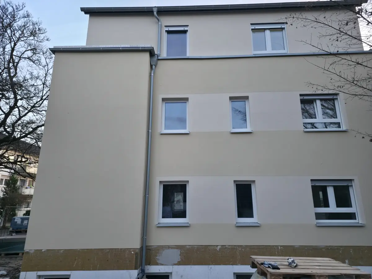 Mehrfamilienhaus mit neuem beigem Außenputz, Sockelbereich noch in Arbeit