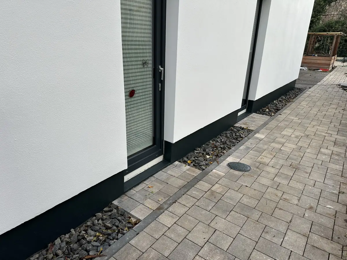 Fertige weiße Putzfassade mit anthrazitfarbenem Sockel und gepflastertem Weg