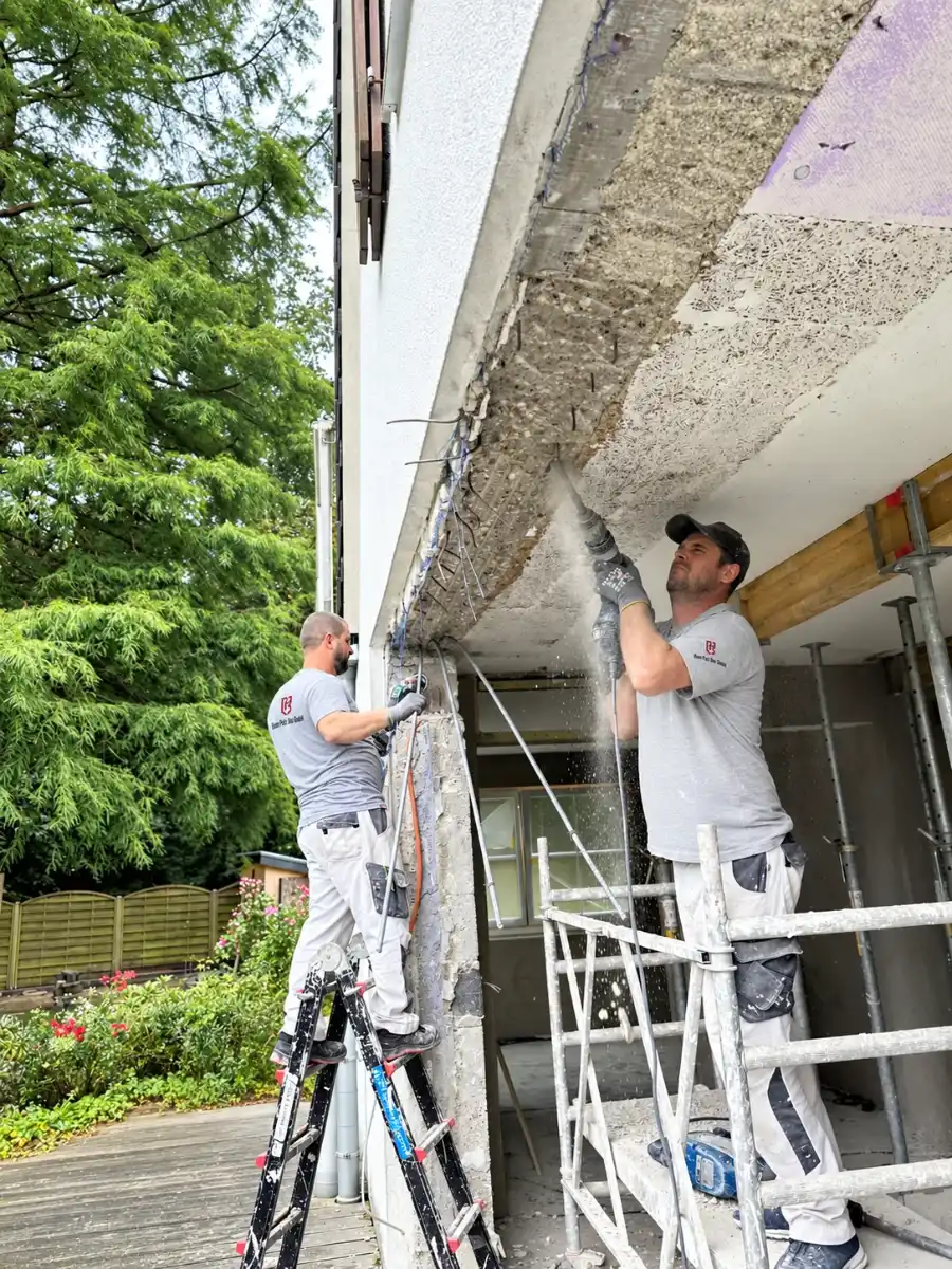 Mitarbeiter von Bonn Putz Bau bearbeiten die Betonunterseite eines Balkons bei einer Sanierung