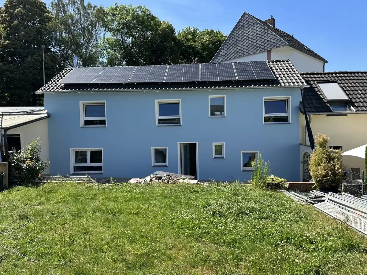 Sanierte hellblaue Fassade eines Wohnhauses mit Garten
