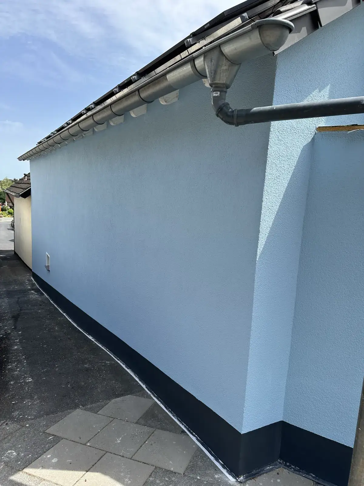 Hellblau verputzte Hauswand mit dunklem Sockel