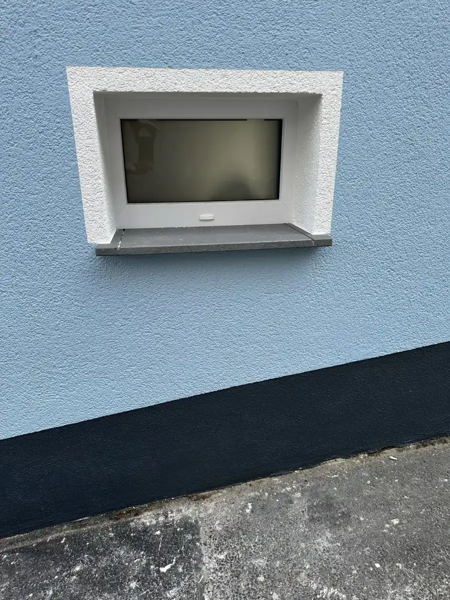 Kellerfenster mit verputzter Laibung in hellblauer Fassade