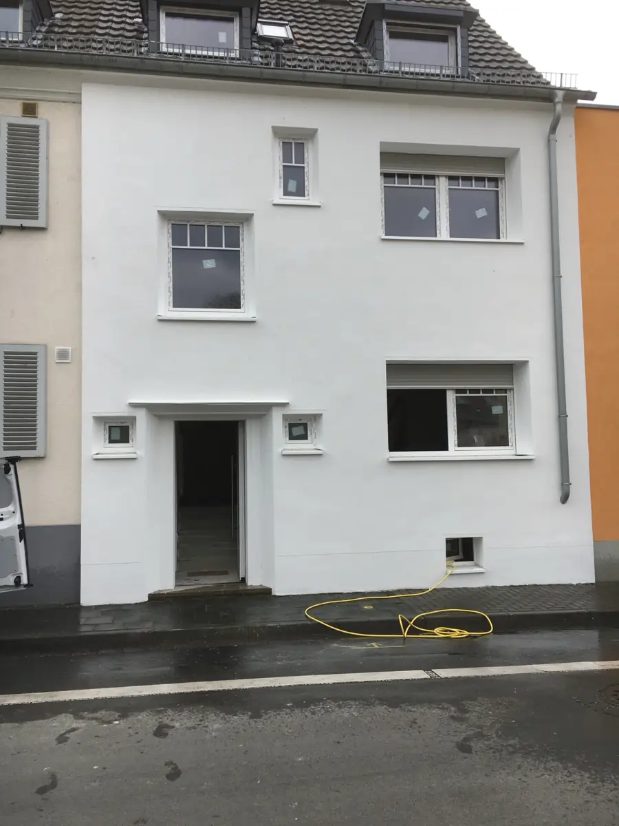 Sanierte weiße Fassade eines Reihenhauses mit neuen Fenstern