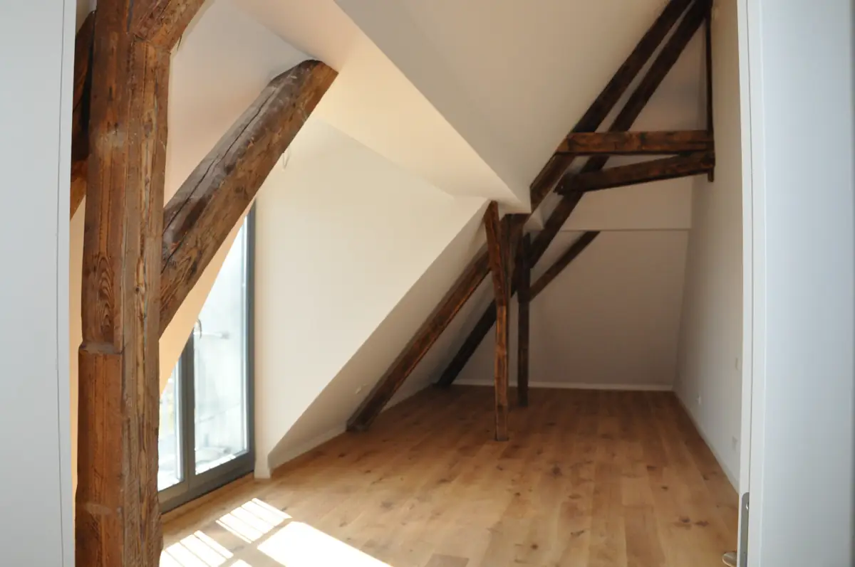 Ausgebautes Dachgeschoss mit historischen Holzbalken, weißen Wänden und Eichenparkett