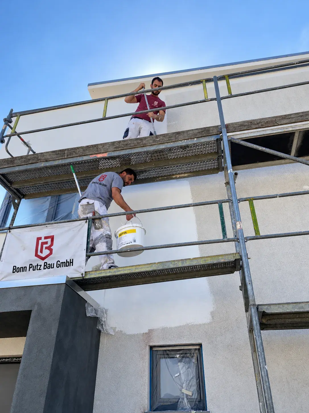 Verputzer von Bonn Putz Bau auf dem Gerüst an einer Fassade mit Firmenbanner