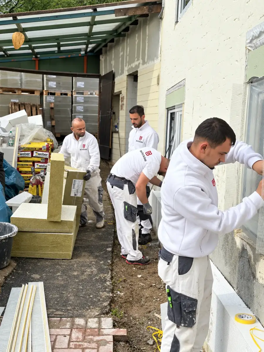 Mitarbeiter von Bonn Putz Bau kleben Mineralwolle-Dämmplatten an eine Hausfassade